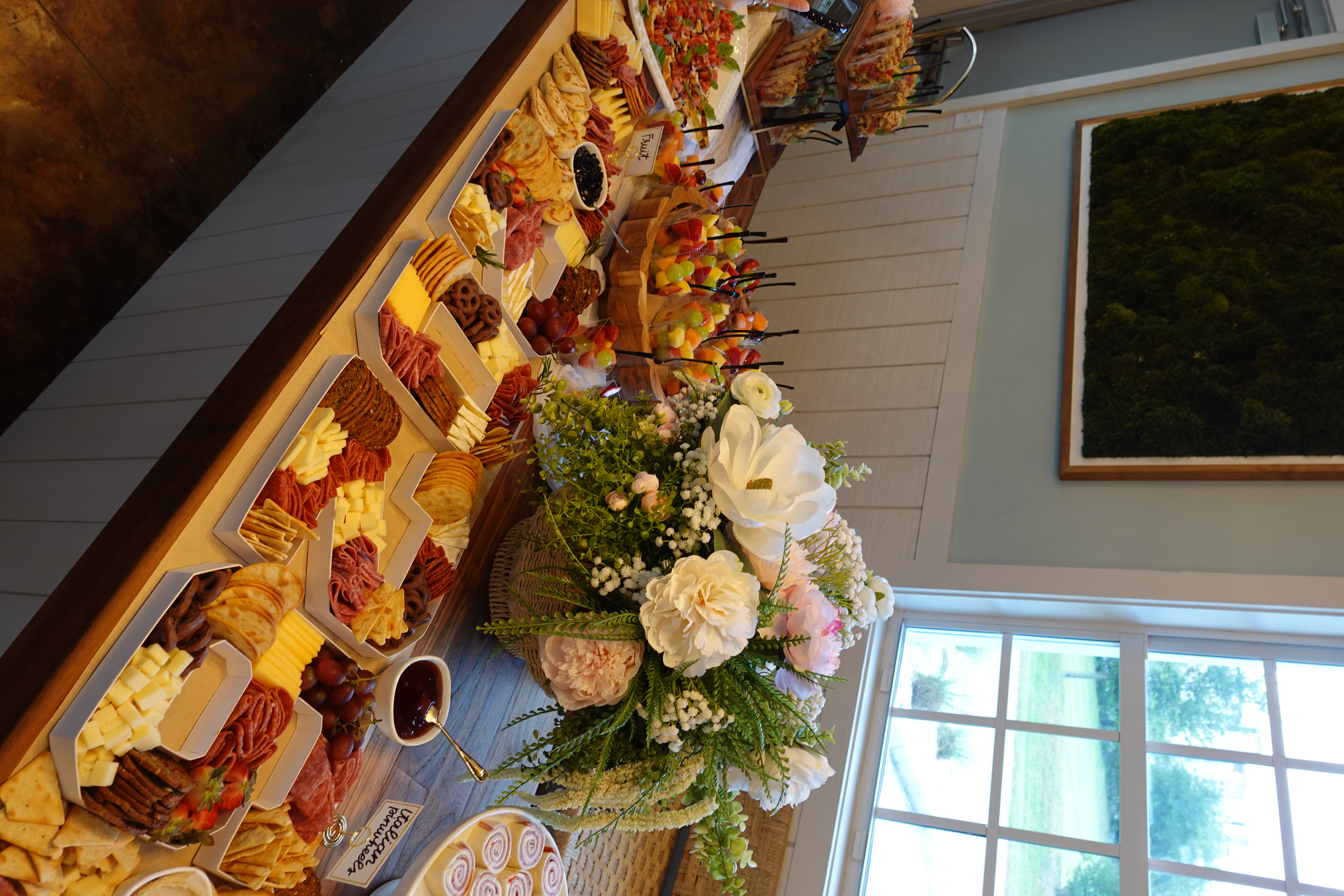 Full grazing table spread with charcuterie, fruits, cheeses, and floral decor at a Palm Ave Catering event