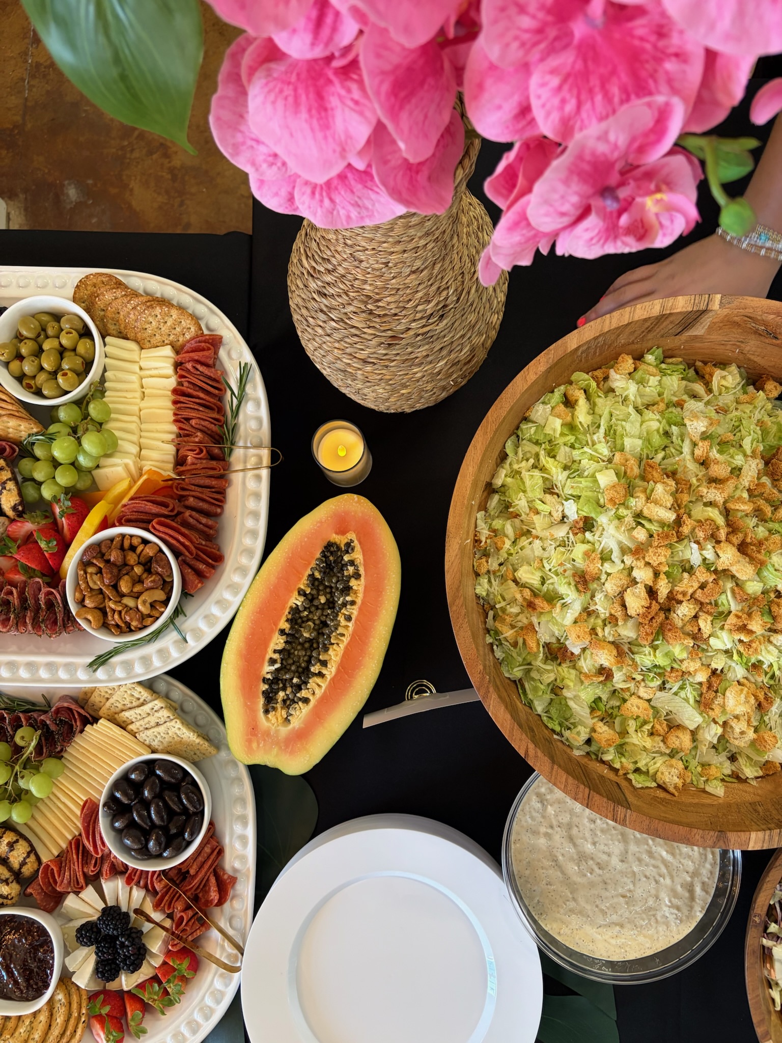 Overhead view of tropical catering event with charcuterie, caesar salad, and pink orchids